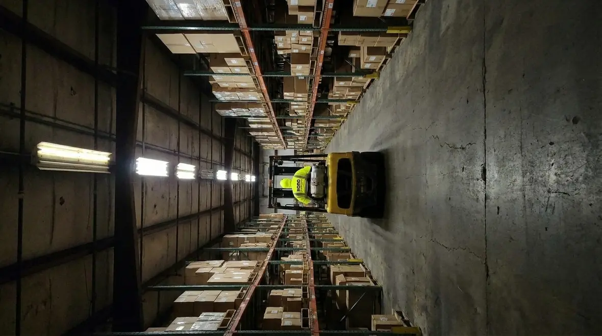 Technicians performing warehouse lighting efficiency upgrades in a busy aisle