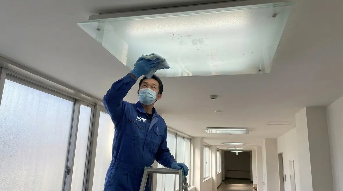 Technician performing commercial building lighting preventive maintenance in a hallway