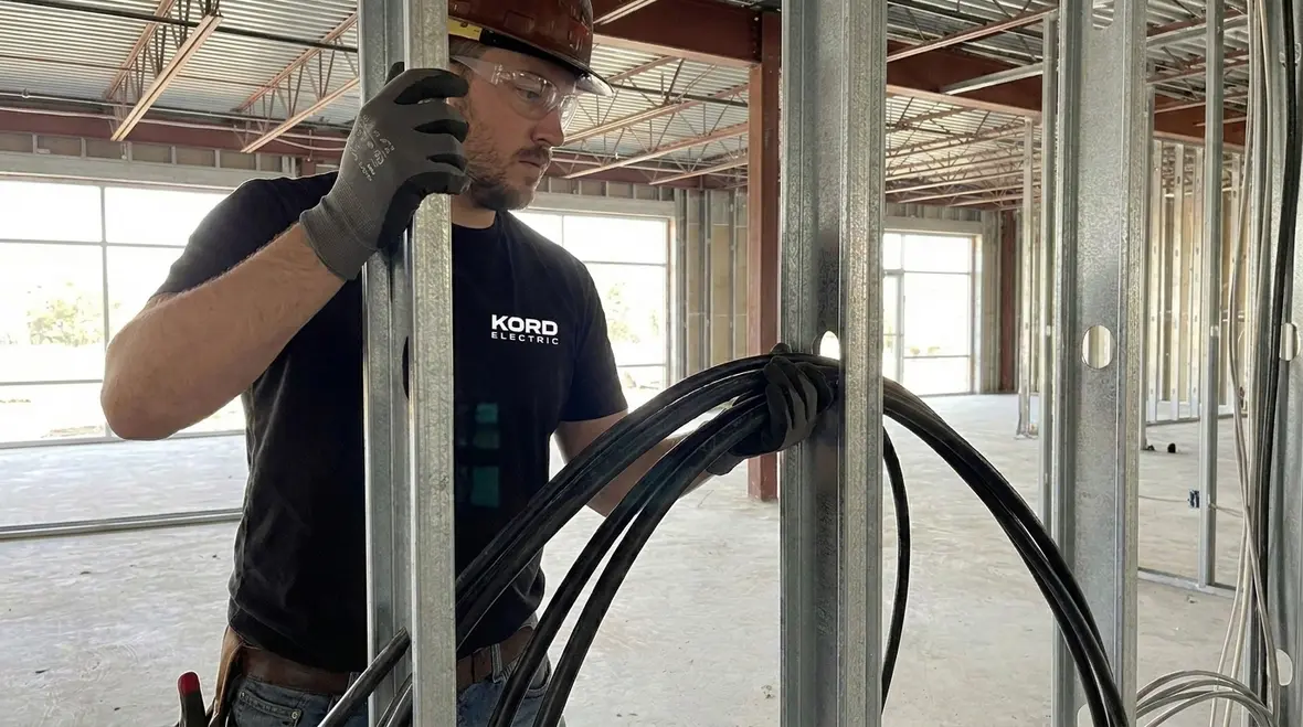 Electrician inspecting NEC SEC cables through framing members in a commercial building