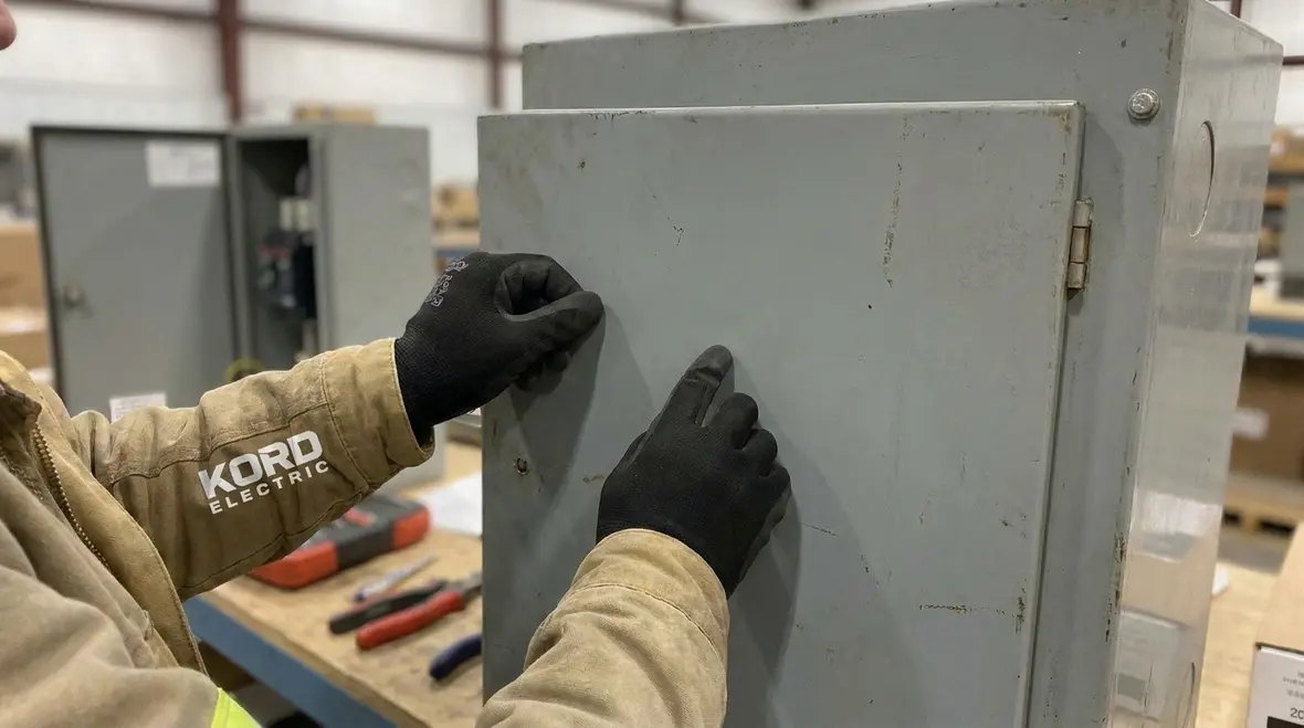 Technician reviewing NEC available fault current marking rules on commercial switchgear